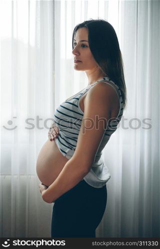 Pregnant holding her nacked belly in front of a curtain. Pregnant holding her nacked belly