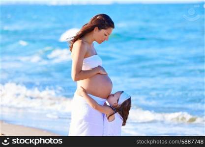 Pregnant mother and daughter on the beach together kissing belly