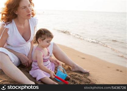pregnant mother and daughter playing in beach sand of Mediterranean