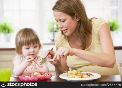 Pregnant mother in kitchen eating chicken and vegetables helping daughter eat