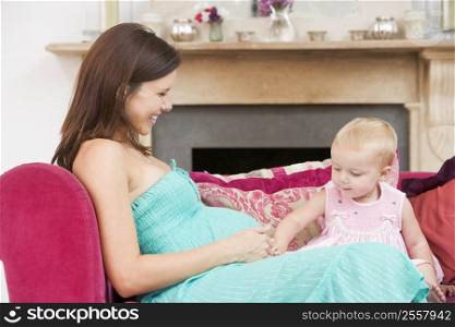 Pregnant mother with daughter in living room touching belly and smiling