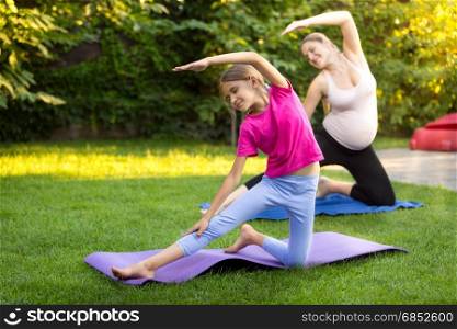 Pregnant mother with daughter practicing yoga on grass at park