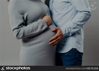 Pregnant wife wears dress poses near husband who touches her big belly. Future mothr and father wait for new member of family. Parenthood concept
