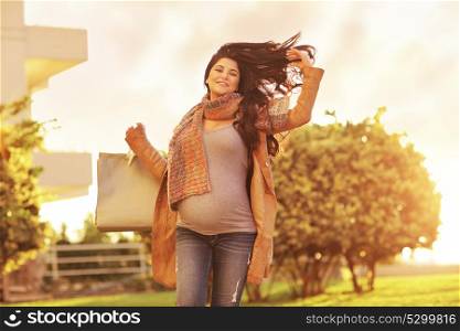 Pregnant woman after shopping, happy expectant girl with paper bags going home, mild sunset light, enjoying great autumn sale