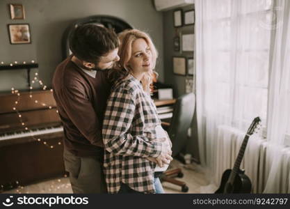 Pregnant woman and happy man in the house standing hugged in the room