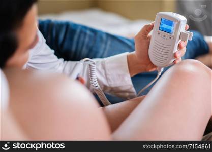 pregnant woman and her husband using fetal droppler device for listening her baby heartbeat