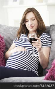Pregnant Woman At Home Drinking Glass Of Red Wine