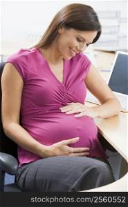 Pregnant woman at work holding belly and smiling