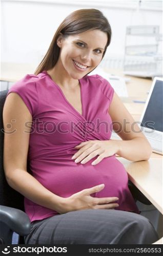 Pregnant woman at work holding belly and smiling