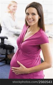 Pregnant woman at work holding belly smiling with coworker in background