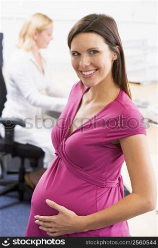 Pregnant woman at work holding belly smiling with coworker in background