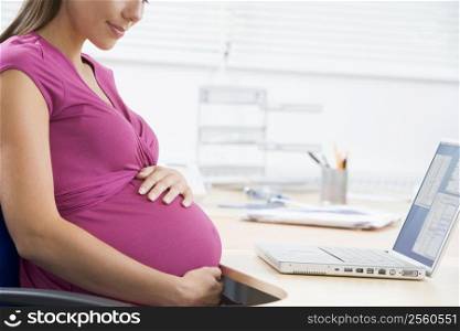 Pregnant woman at work with laptop holding belly and smiling