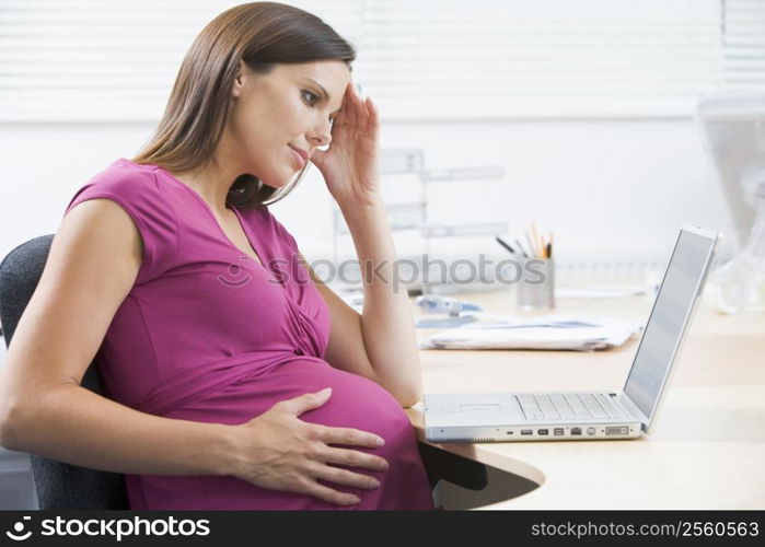 Pregnant woman at work with laptop looking stressed