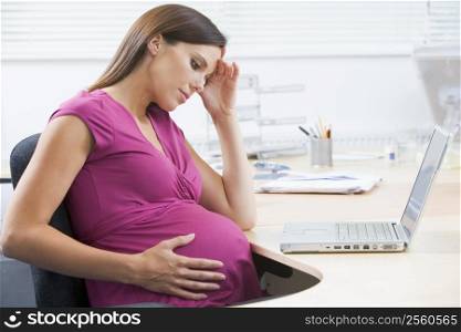Pregnant woman at work with laptop looking stressed