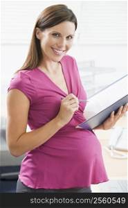 Pregnant woman at work writing in binder smiling