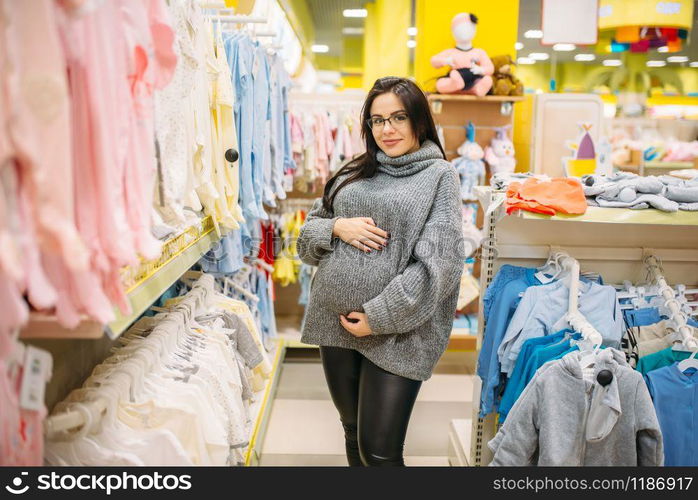 Pregnant woman buying clothes in the store for newborns. Future mother in shop of goods for infants