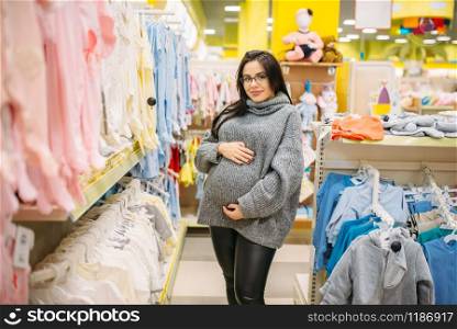 Pregnant woman buying clothes in the store for newborns. Future mother in shop of goods for infants