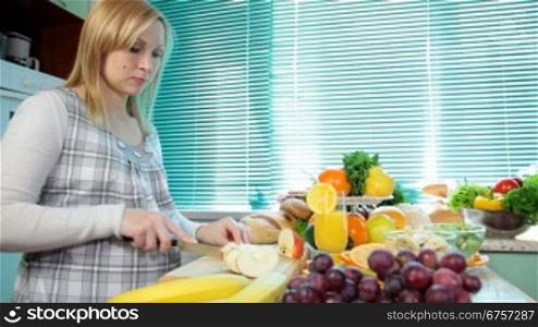 Pregnant woman cutting apple for the fruit salad in the kitchen