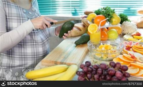 Pregnant woman cutting avocado in the kitchen