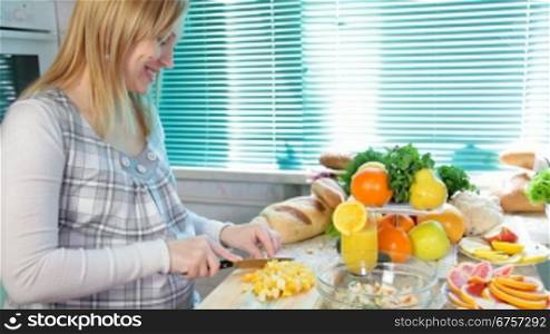 Pregnant woman cutting orange for the fruit salad in the kitchen