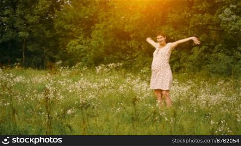 Pregnant woman dancing in the field at sunset