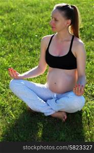 Pregnant woman doing yoga outdoors at sunny summer day