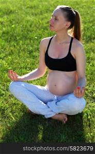 Pregnant woman doing yoga outdoors at sunny summer day