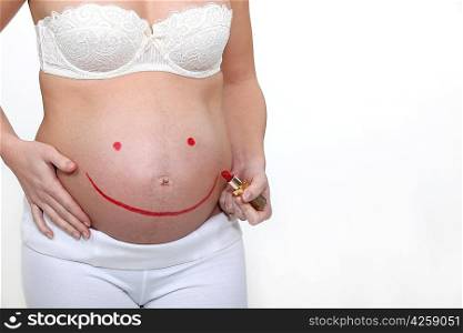 Pregnant woman drawing a smile on her belly with a lipstick