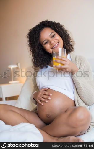 Pregnant woman drinking orange juice in bedroom