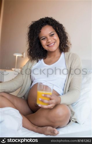 Pregnant woman drinking orange juice in bedroom