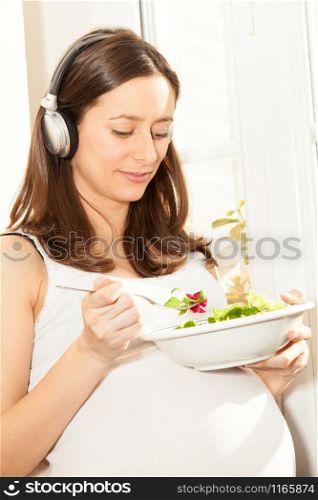 pregnant woman eat salad and listening to music