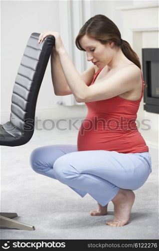 Pregnant Woman Exercsing Using Back Of Chair At Home