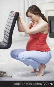 Pregnant Woman Exercsing Using Back Of Chair At Home