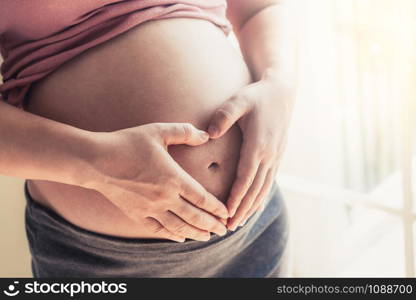 Pregnant woman feeling happy at home while taking care of her child. The young expecting mother holding baby in pregnant belly. Maternity prenatal care and woman pregnancy concept.