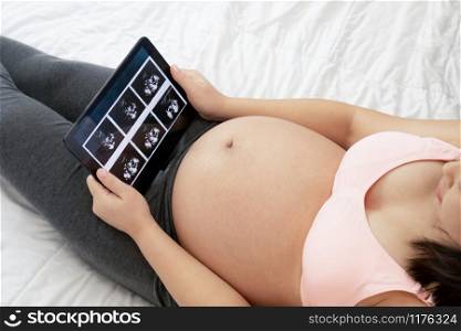 Pregnant woman feeling happy at home while taking care of her child. The young expecting mother holding baby in pregnant belly. Maternity prenatal care and woman pregnancy concept.. Happy pregnant woman and expecting baby at home.