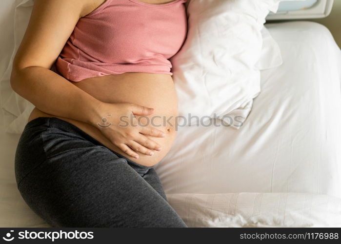 Pregnant woman feeling happy at home while taking care of her child. The young expecting mother holding baby in pregnant belly. Maternity prenatal care and woman pregnancy concept.