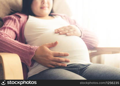 Pregnant woman feeling happy at home while taking care of her child. The young expecting mother holding baby in pregnant belly. Maternity prenatal care and woman pregnancy concept.