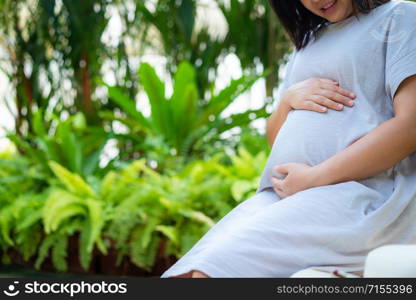 Pregnant woman feeling happy at home while taking care of her child. The young expecting mother holding baby in pregnant belly. Maternity prenatal care and woman pregnancy concept.