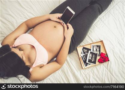 Pregnant woman feeling happy at home while taking care of her child. The young expecting mother holding baby in pregnant belly. Maternity prenatal care and woman pregnancy concept.. Happy pregnant woman and expecting baby at home.
