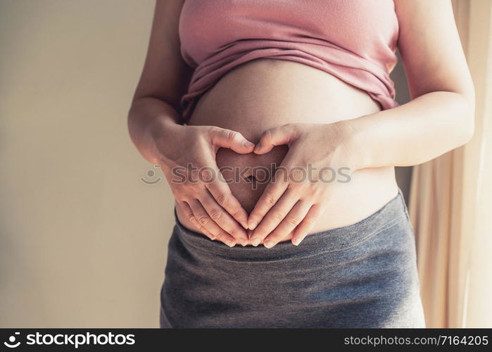 Pregnant woman feeling happy at home while taking care of her child. The young expecting mother holding baby in pregnant belly. Maternity prenatal care and woman pregnancy concept.