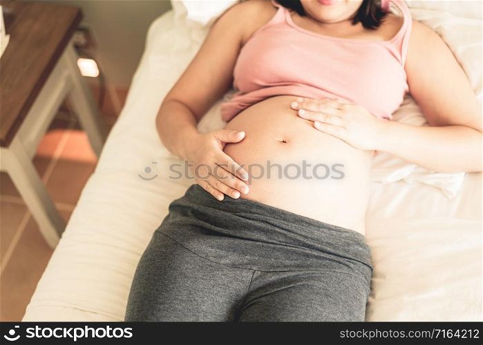 Pregnant woman feeling happy at home while taking care of her child. The young expecting mother holding baby in pregnant belly. Maternity prenatal care and woman pregnancy concept.