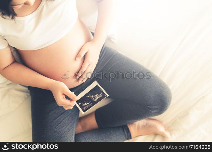 Pregnant woman feeling happy at home while taking care of her child. The young expecting mother holding baby in pregnant belly. Maternity prenatal care and woman pregnancy concept.