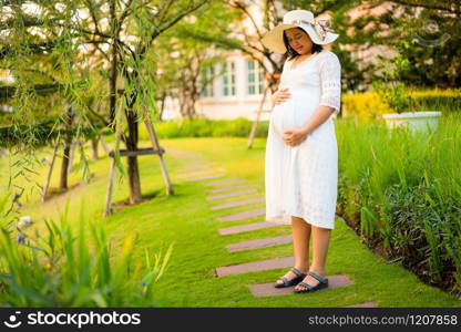 Pregnant woman feeling happy with new life at garden home while take care of her child. The young expecting mother holding baby in pregnant belly. Maternity prenatal care and woman pregnancy concept.