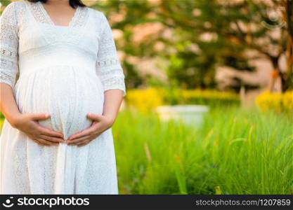 Pregnant woman feeling happy with new life at garden home while take care of her child. The young expecting mother holding baby in pregnant belly. Maternity prenatal care and woman pregnancy concept.