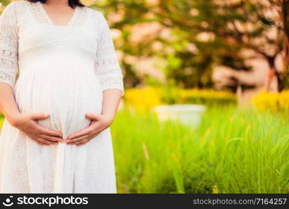 Pregnant woman feeling happy with new life at garden home while take care of her child. The young expecting mother holding baby in pregnant belly. Maternity prenatal care and woman pregnancy concept.