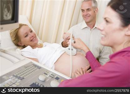 Pregnant woman getting ultrasound from doctor with husband watching