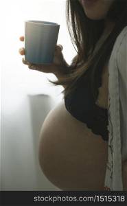 Pregnant woman holding a mug drinking in the morning