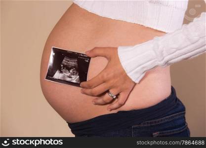 Pregnant woman holding an ultrasound photo on her exposed tummy