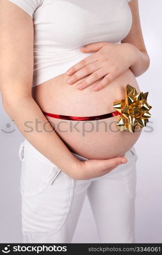 Pregnant woman holding belly wrapped around with red ribbon and golden bow as a gift