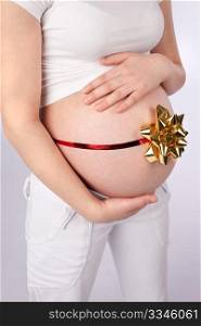 Pregnant woman holding belly wrapped around with red ribbon and golden bow as a gift